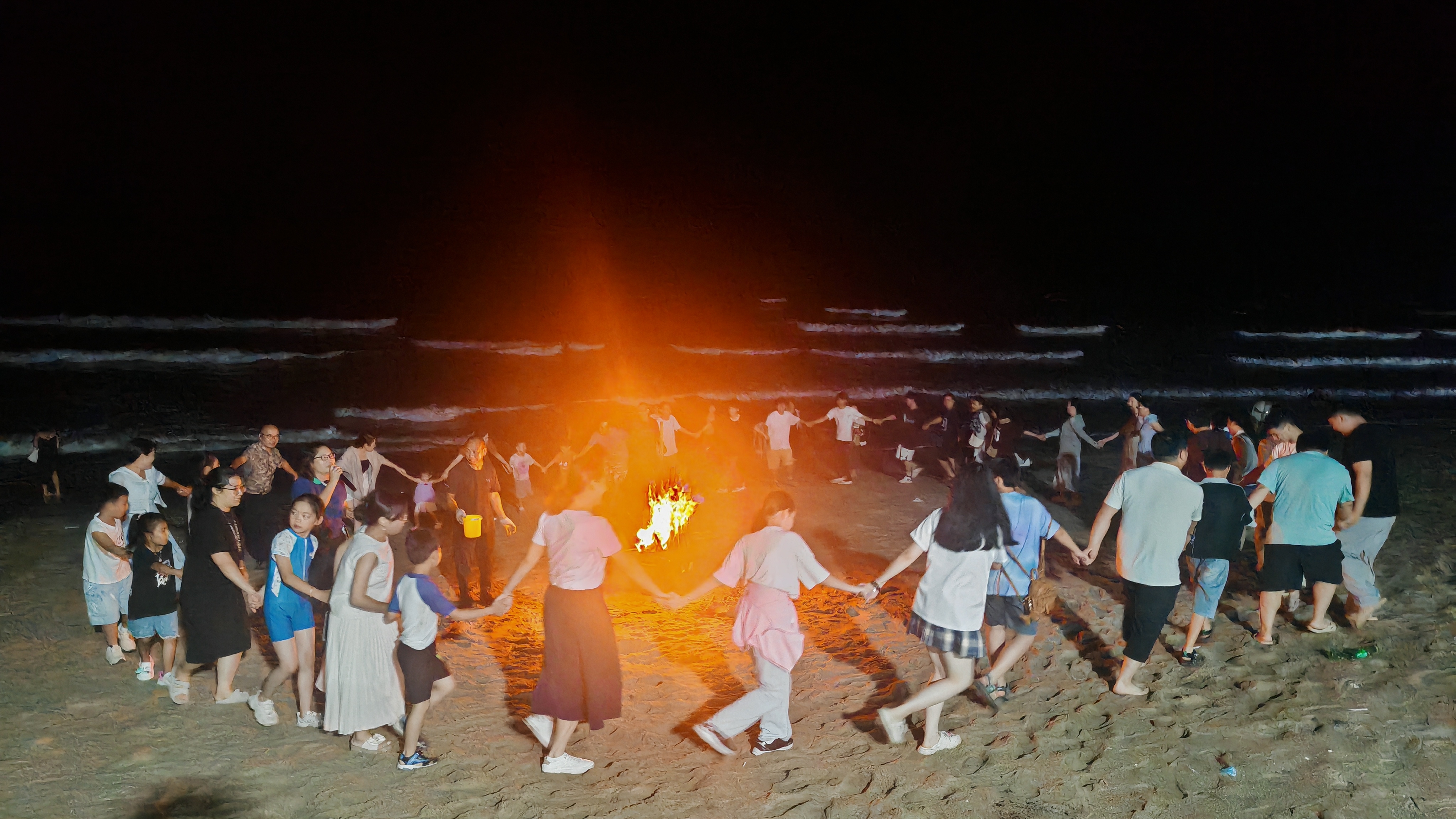 Team gathered around a bonfire on Shuangyue Bay beach at sunset